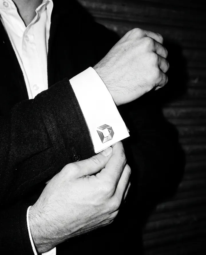 Close crop of a hand fixing a white French cuff closed with a steel D cufflink, at night.